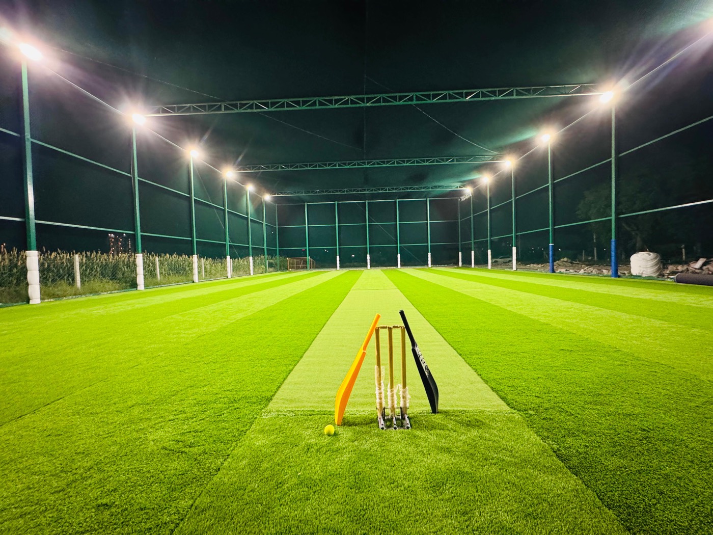 Turf cricket pitch with stumps under floodlights